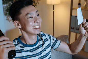 Young man watching tv with lottery ticket in hand