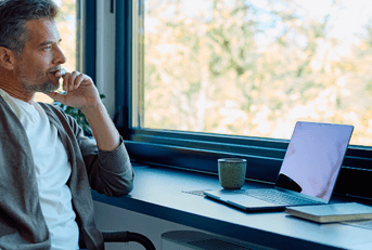 Man thinking with laptop near window