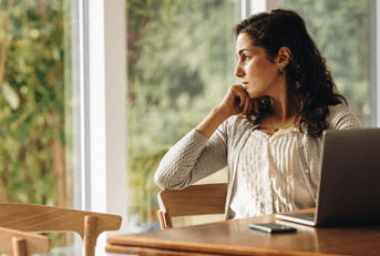 Woman thinking near window with her computer