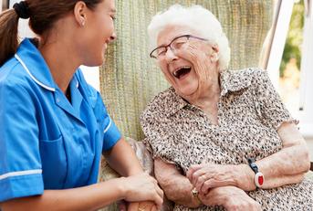 happy senior woman and nurse sitting in chair