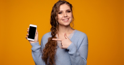 smiling young woman wearing grey sweatshirt holding smartphone