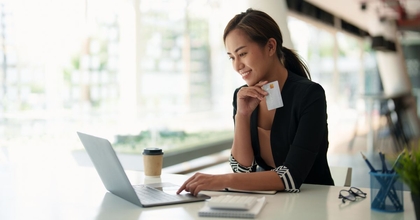 Happy women online banking on laptop holding debit card