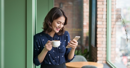 Woman smiling and holding a cup of coffee while looking at phone