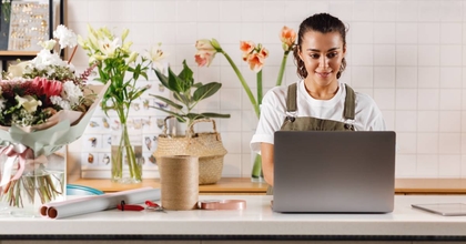 Young flower shop owner using laptop on counter while standing.