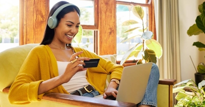 A happy woman sitting on an armchair while using her laptop.