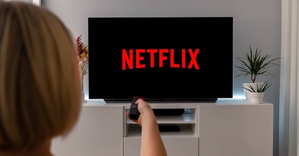 A woman holds up her remote control pointing to her TV, which is showing the Netflix screen.