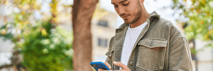 A young person looks down at their phone while standing outside.