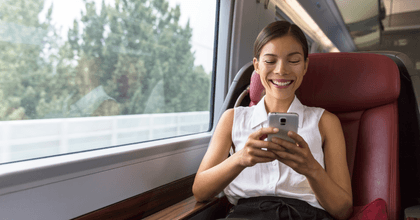 A woman smiles while playing on her phone on a train.