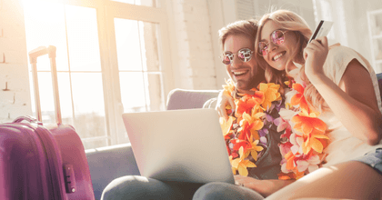 A man and woman wear leis and use a laptop to book their tickets.