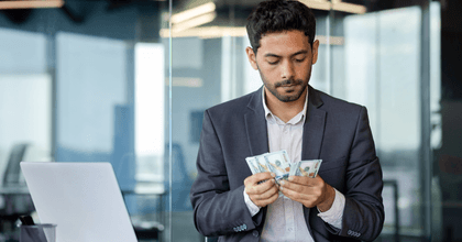 A man counts his cash while sitting in front of his laptop at the office.