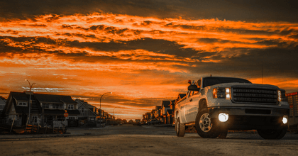 A white GMC Sierra is shown with its headlights on against an orange sky.