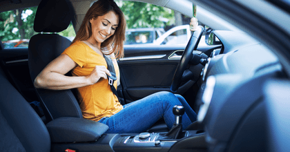 A woman in an orange shirt smiles as she puts on her seatbelt.