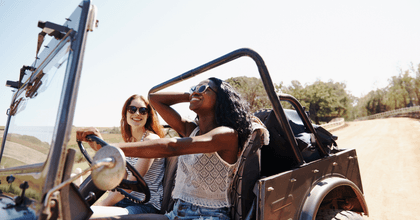 Two women in a convertible SUV drive down a road on a bright, sunny day.