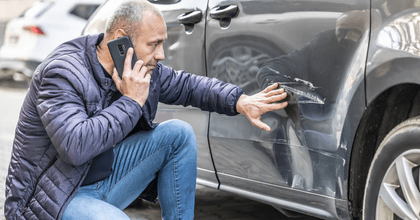Man looking at car with dent