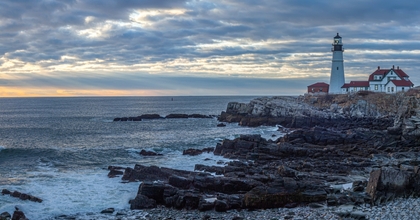 Maine lighthouse in background with ocean shoreline in foreground