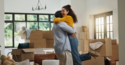Young couple hugging and celebrating with boxes stacked around them in new house
