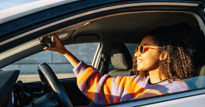 A woman in a striped sweater adjusts her rearview mirror in her car.