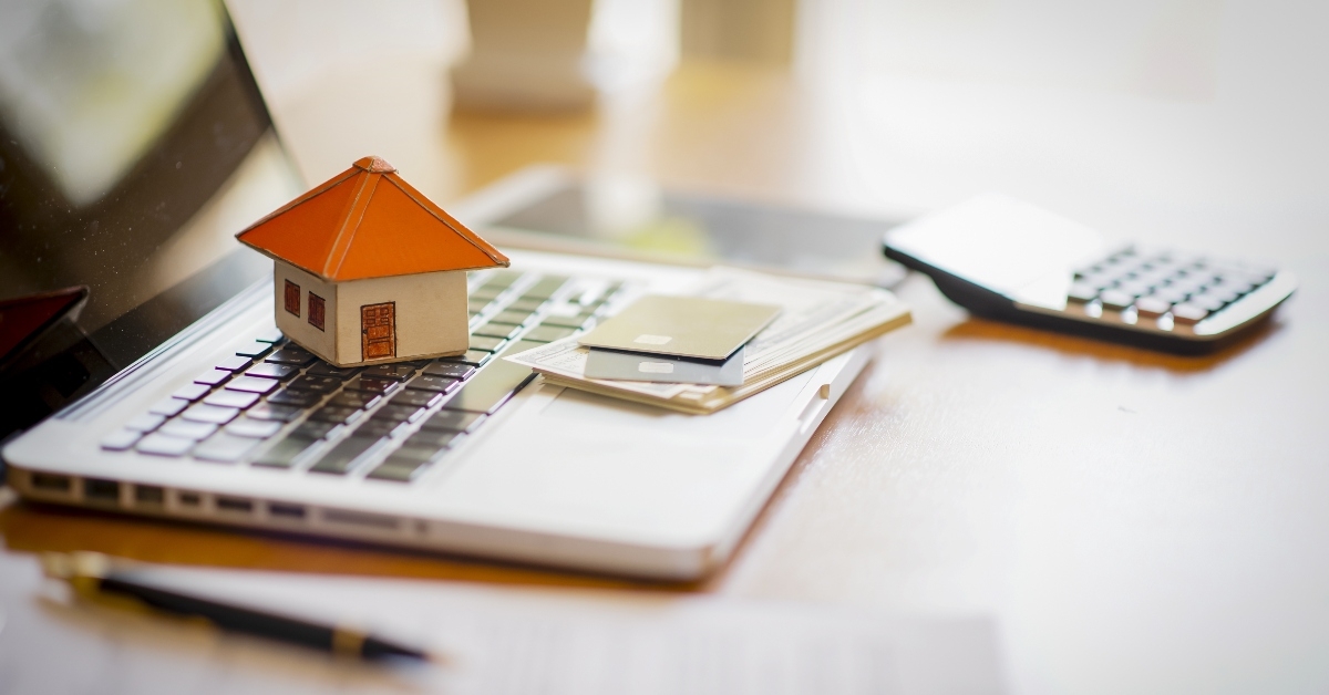 Laptop next to calculator and tiny wooden house