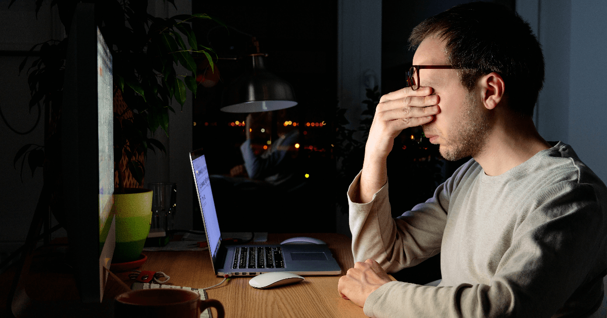 Tired man rubbing his eyes, sitting at desktop PC/laptop late at night 