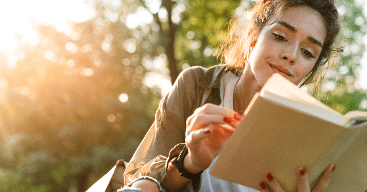 woman smiling and reading book in green park 