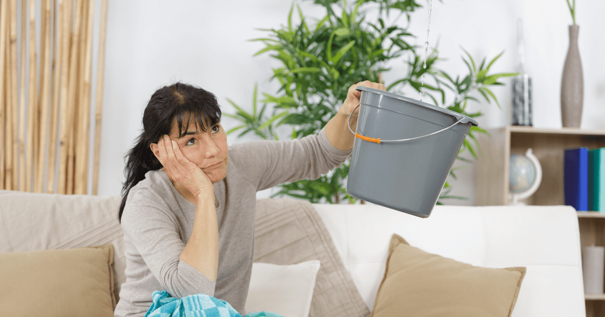 Woman holding bucket to stop roof leak