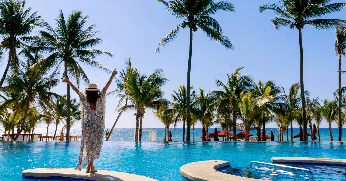 Woman standing in front of pool with palm trees around
