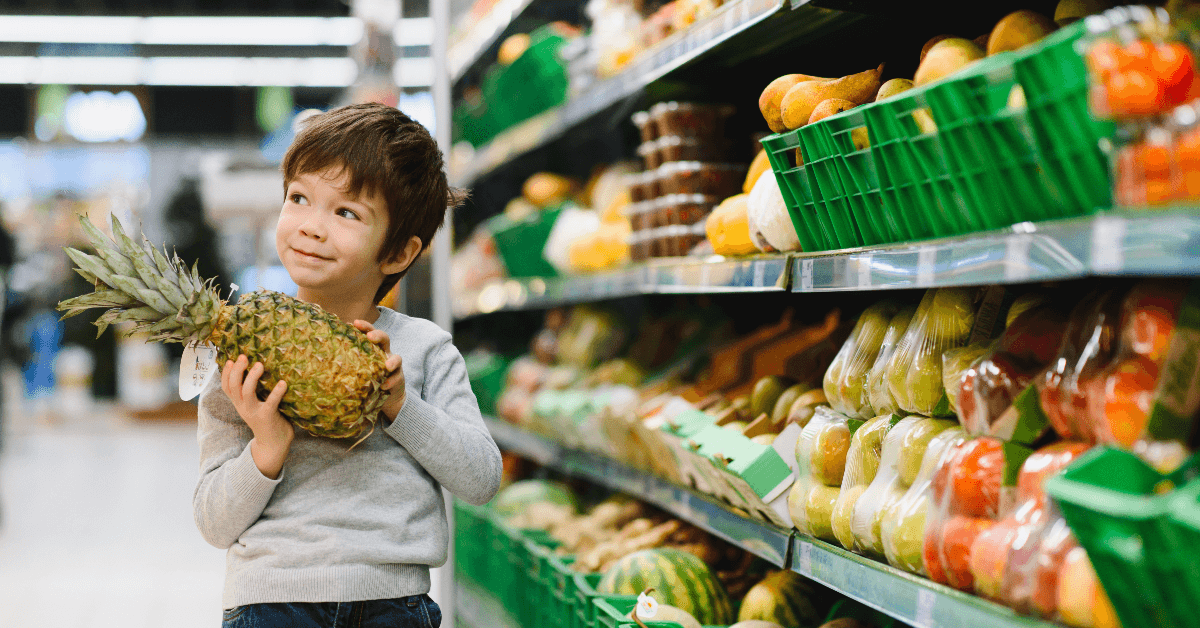 Little boy holding pineapple in grocery store