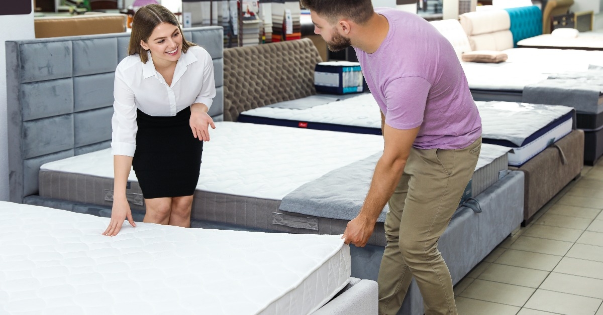 saleswoman helping customer to choose new mattress in store
