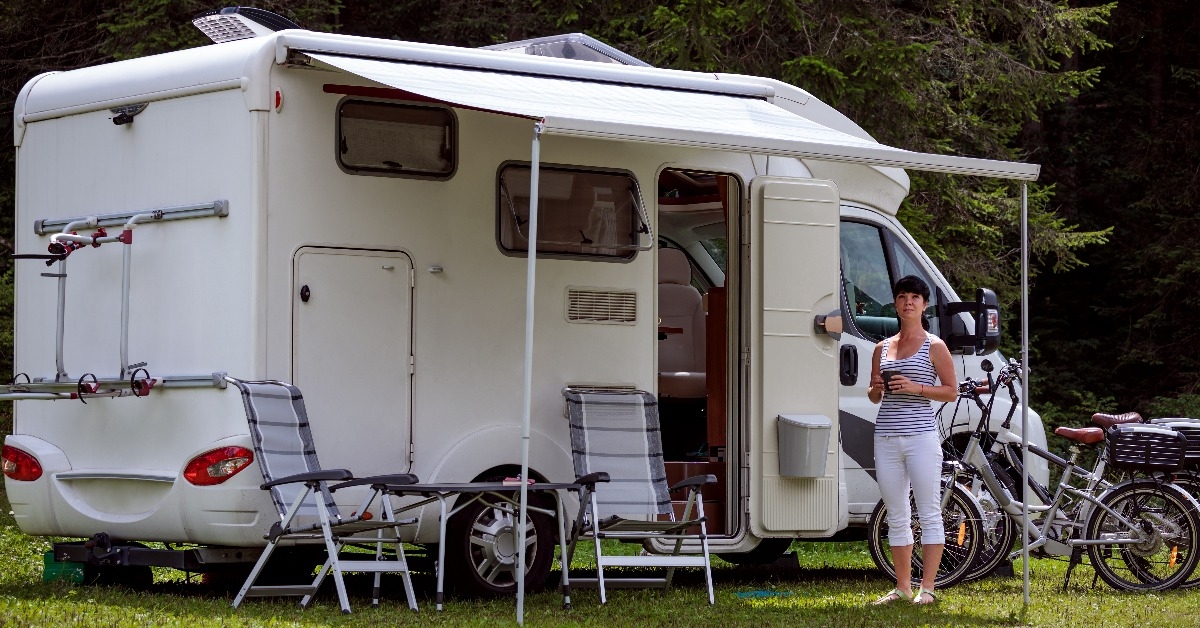 woman is standing with a mug of coffee near the camper RV