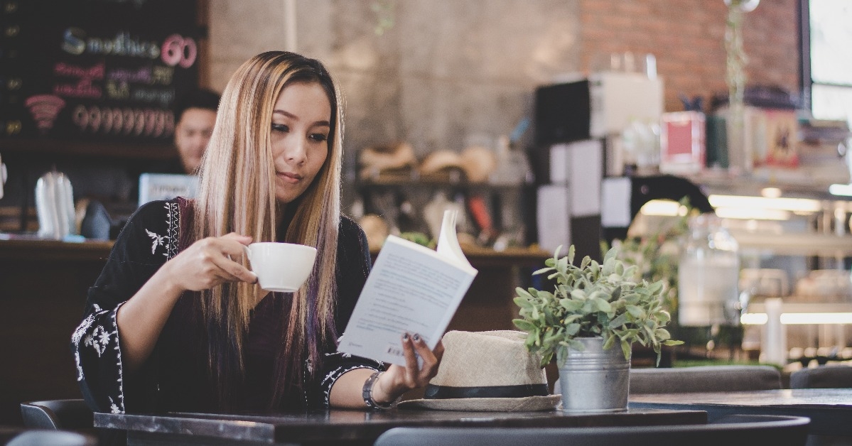 happy business woman reading book while relaxing at cafe