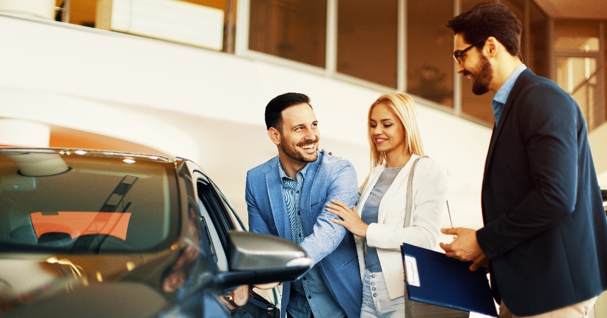 young couple choosing new car for buying in dealership shop