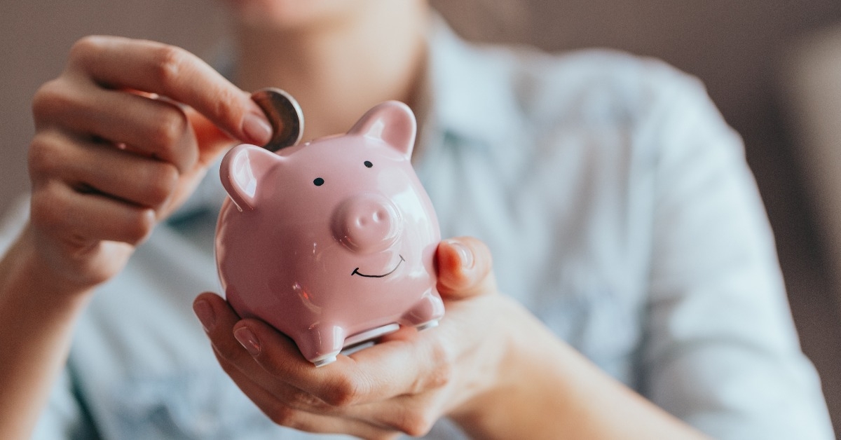 female hands hold a pink piggy bank and puts a coin