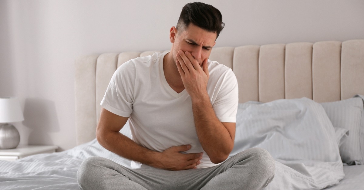 man suffering from nausea on bed at home