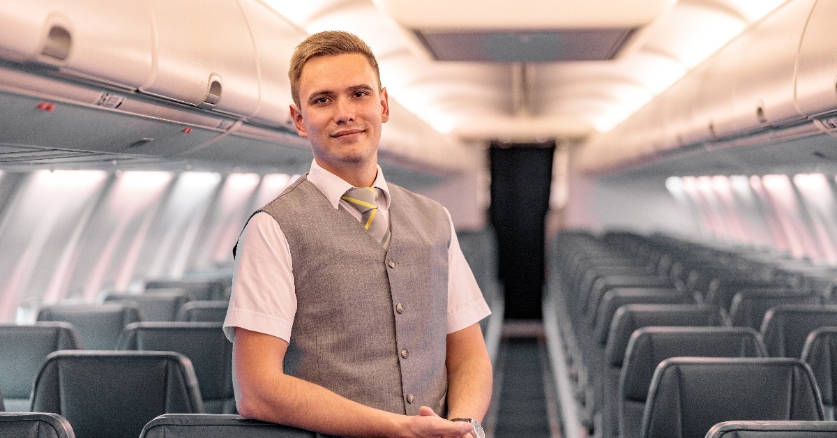 male flight attendant standing in aircraft passenger salon