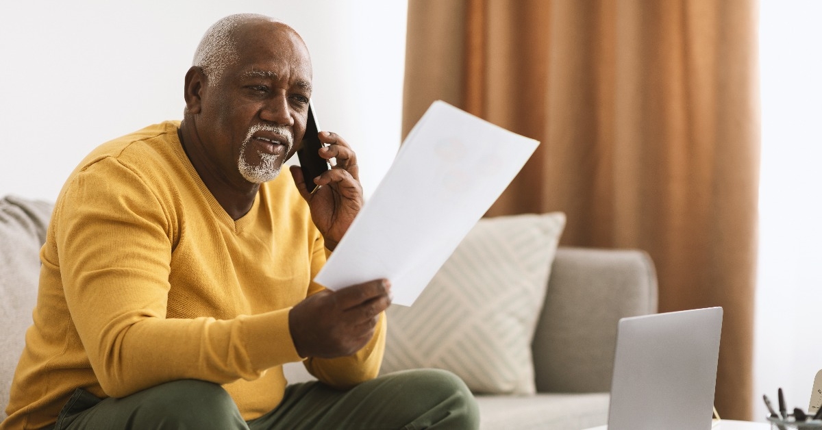 senior black businessman talking on phone holding papers working indoors