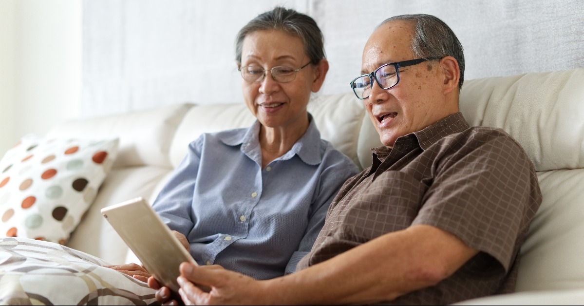 Senior couple sitting on sofa in home playing tablet