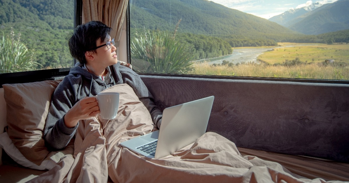 young Asian man drinking hot coffee working with laptop computer inside a campervan