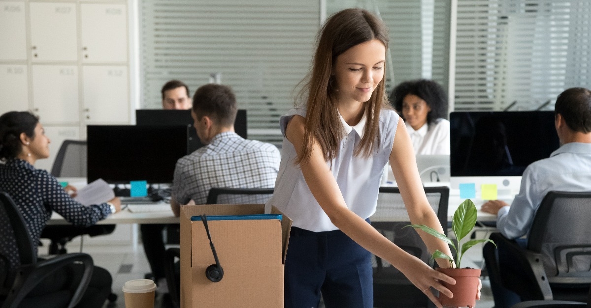 smiling hired female company employee unpacking box with personal belongings at workplace
