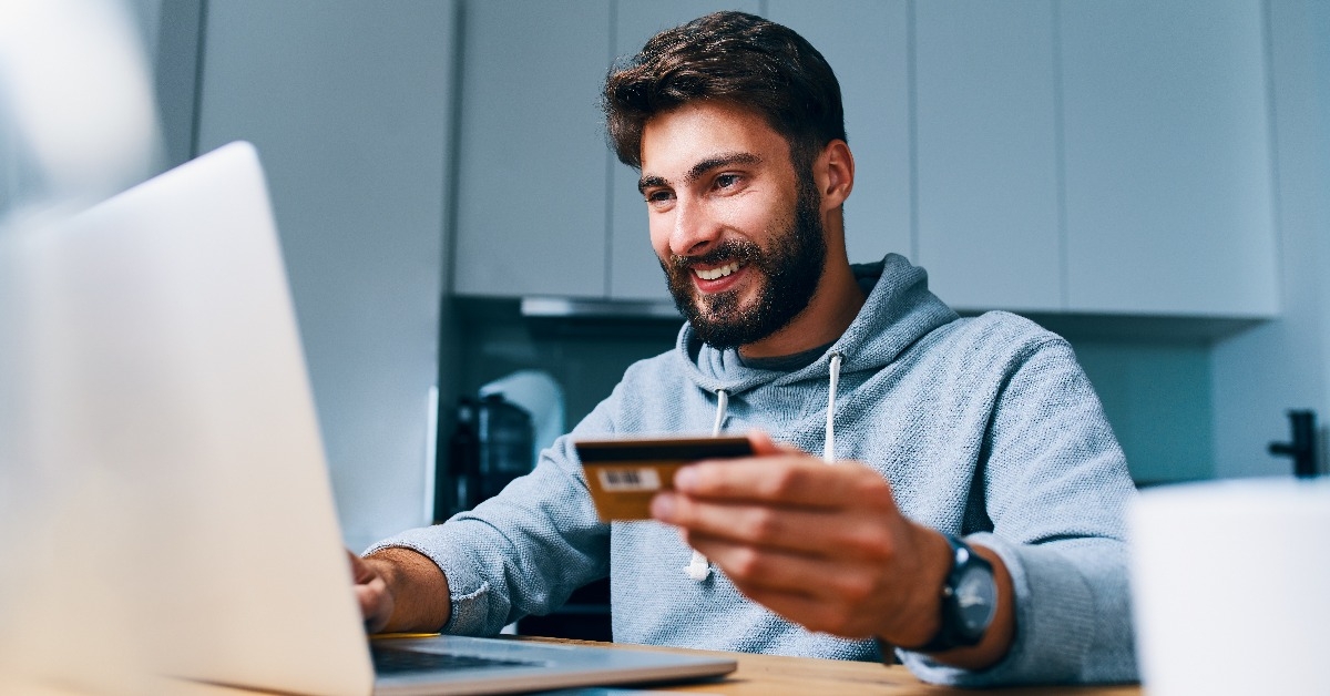 cheerful young man paying bills online with credit card and laptop