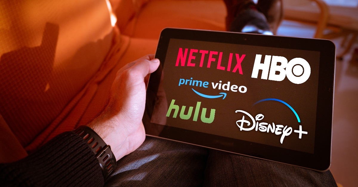 man holds a tablet with streaming companies logo on screen
