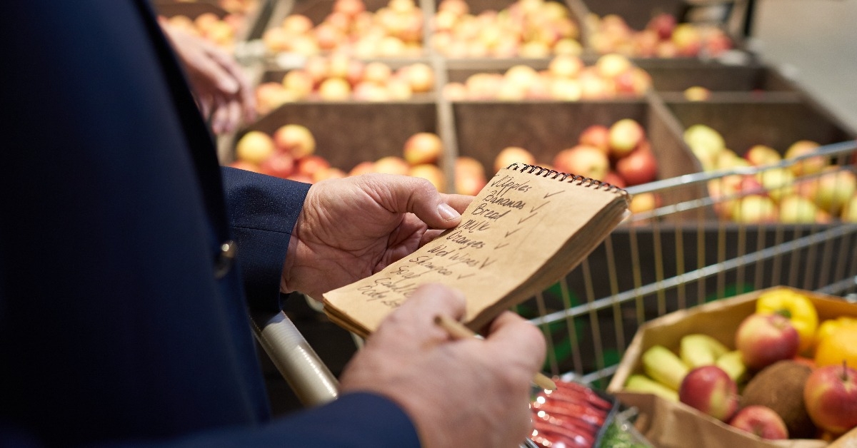 senior man holding shopping list while grocery shopping in supermarket
