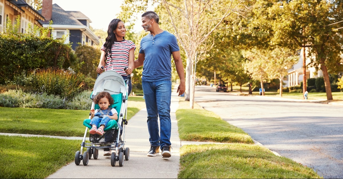 couple push daughter in stroller as they walk along street