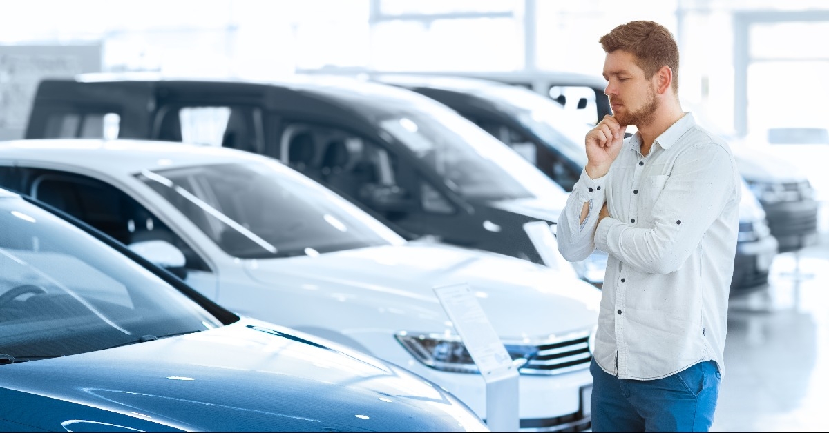 young man standing in front of a new car at the dealership