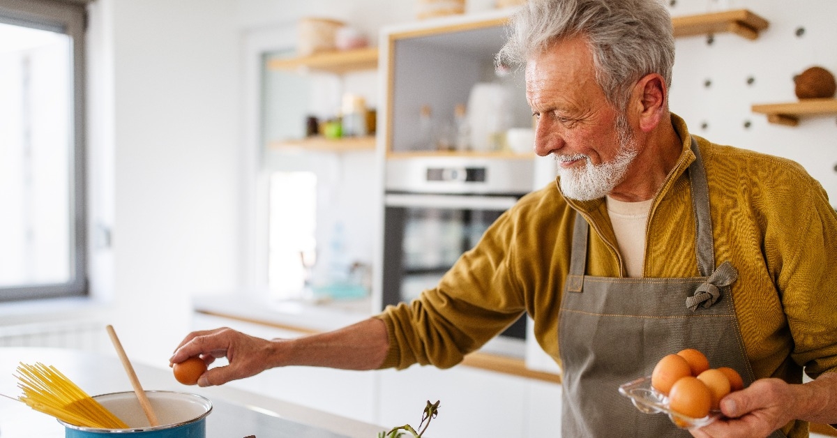 happy retired senior man cooking in kitchen