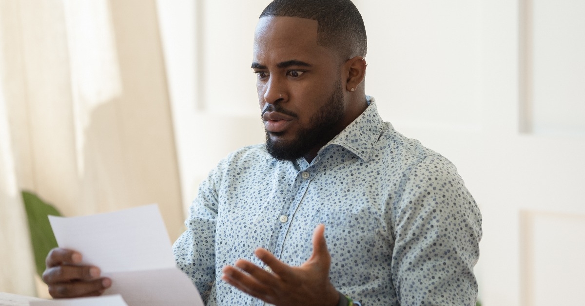 african man sitting at table holding letter reading awful news