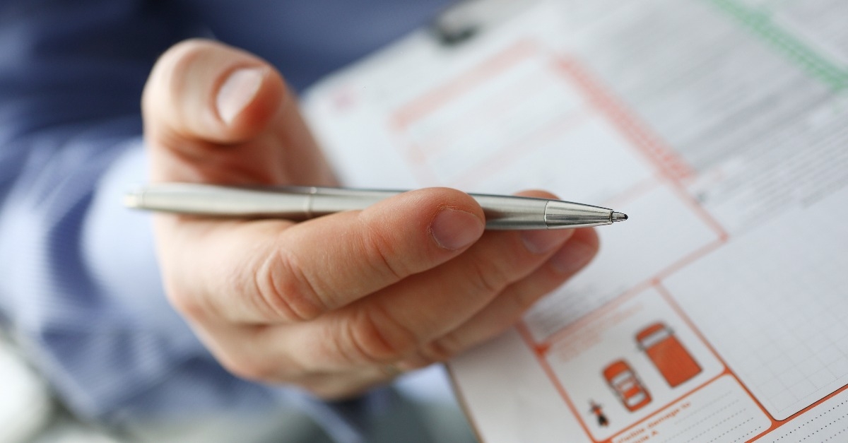 male insurer hand hold silver pen over an accident form