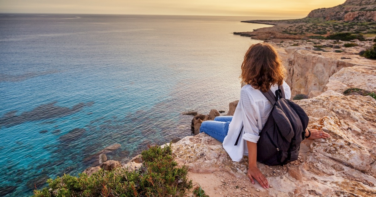 young woman traveler watches a beautiful sunset on the rocks on the beach