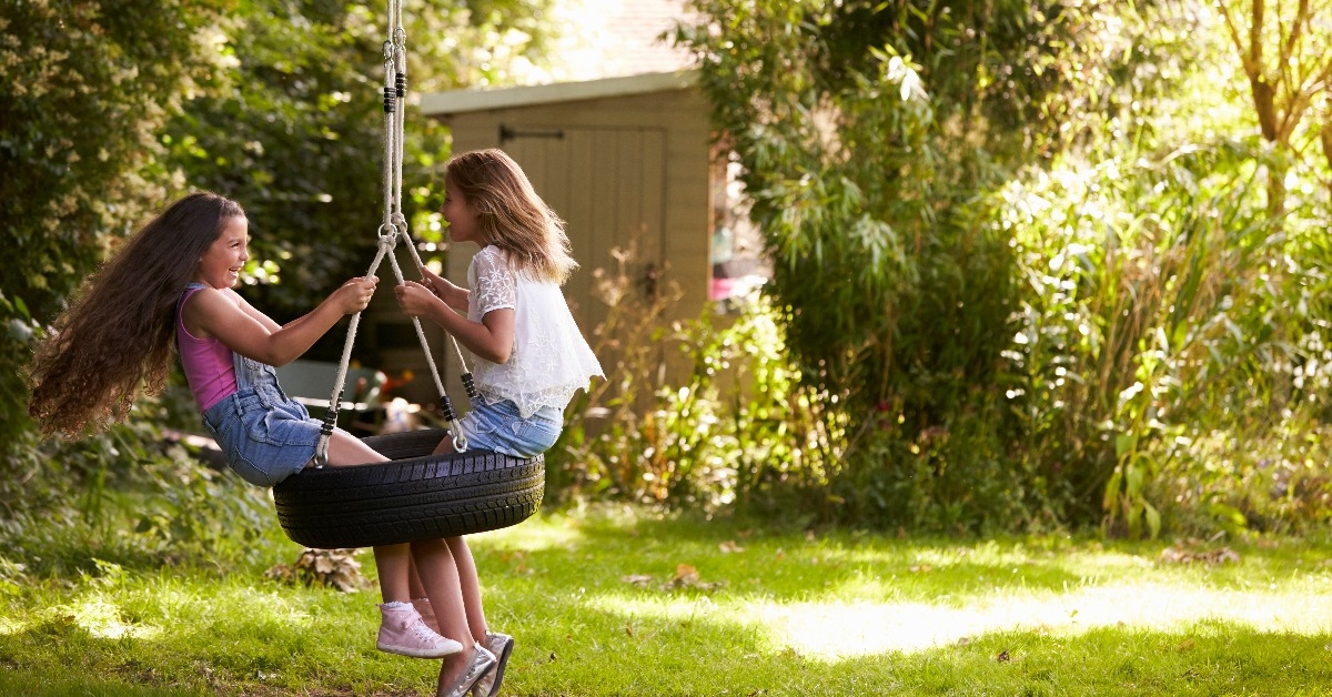 two girls playing together on tire swing in garden