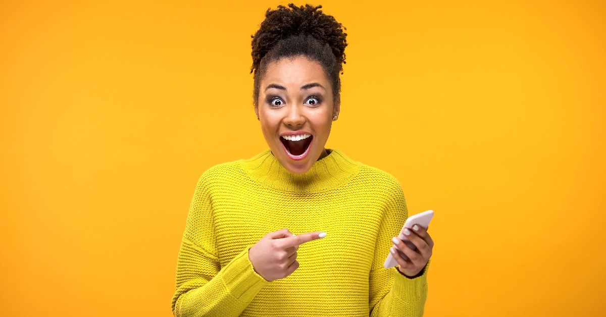 Joyful young woman pointing at smartphone in hand