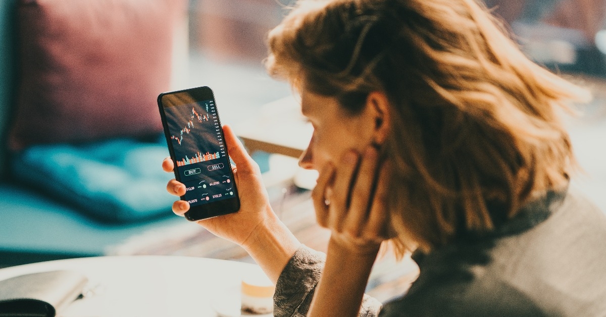 Woman using mobile phone investing application sitting in cafe